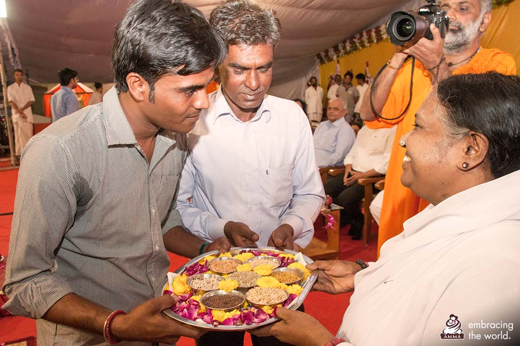 Two men offer a tray of seeds to Amma