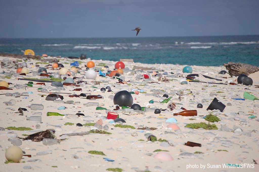 A beach strewn with plastic waste and glass bottles