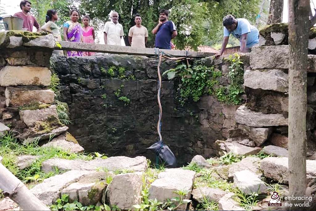 Villagers peer into well as they lower something into it