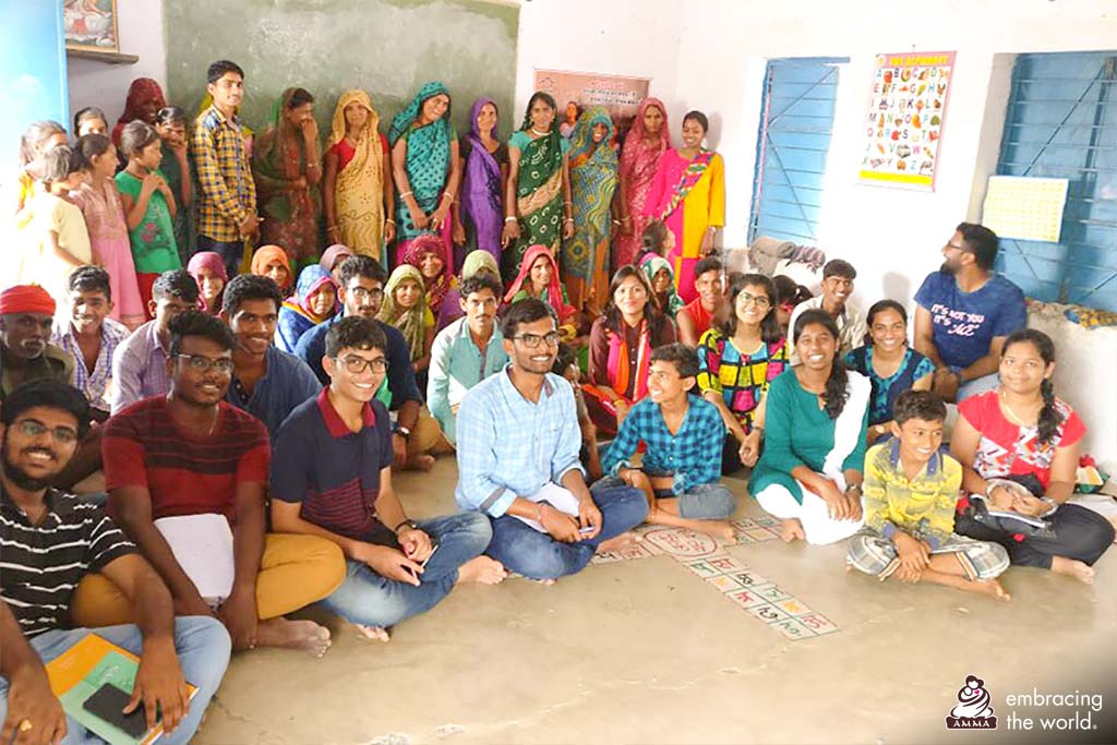 Village children and their parents sit in classroom with college students
