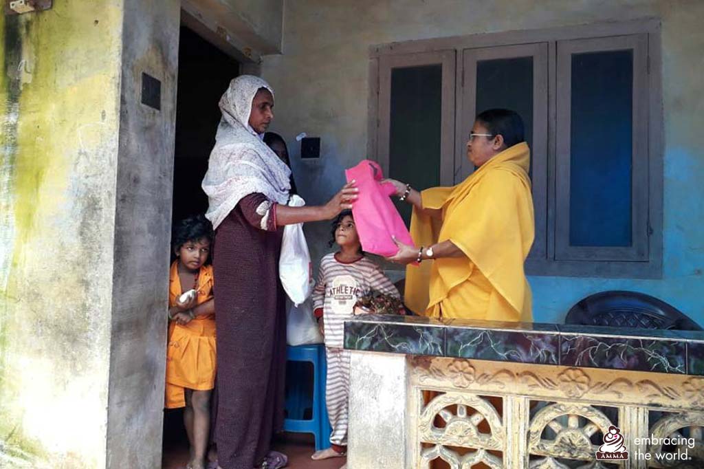 A female monastic hands a bag of supplies to a family at their doorstep