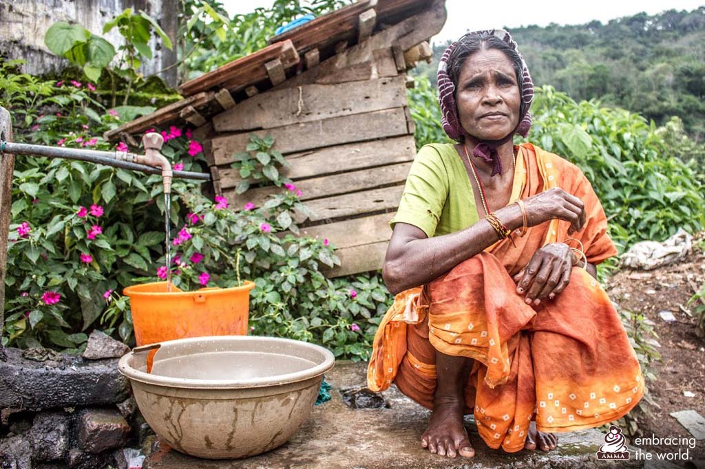 An elderly village woman sits near a water tap
