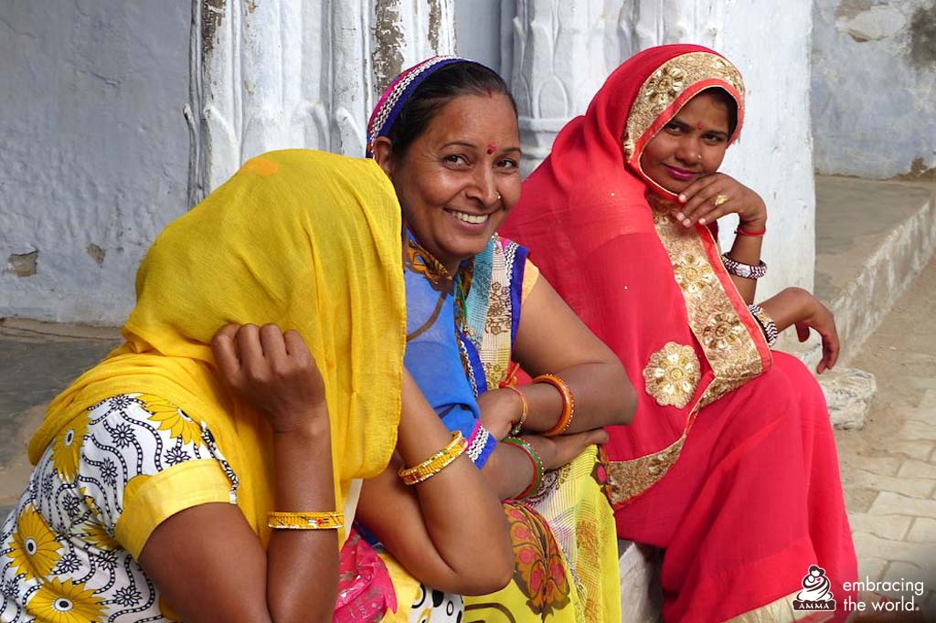 Three Indian women sit together, smiling at camera