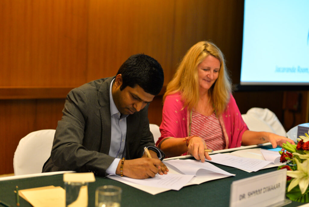 Dr. Shyam sitting down and signing the pledge.   A woman is sitting next to him.