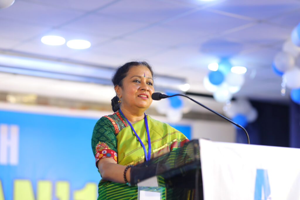 Speaker in green sari stands at podium.