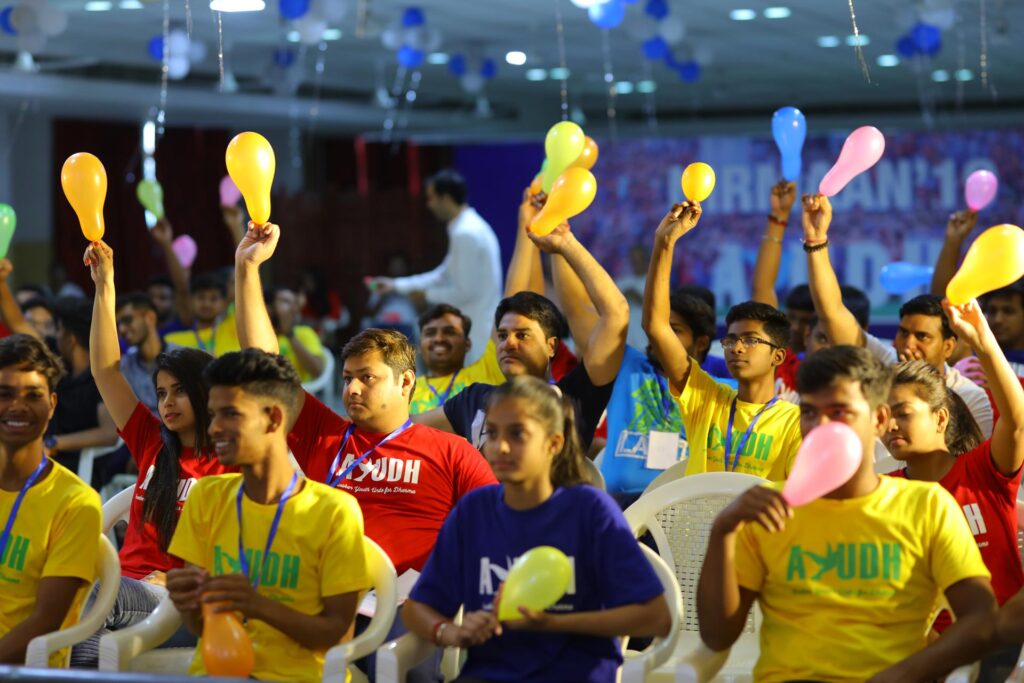 Youth participants seated in the crowd wave balloons in the air.