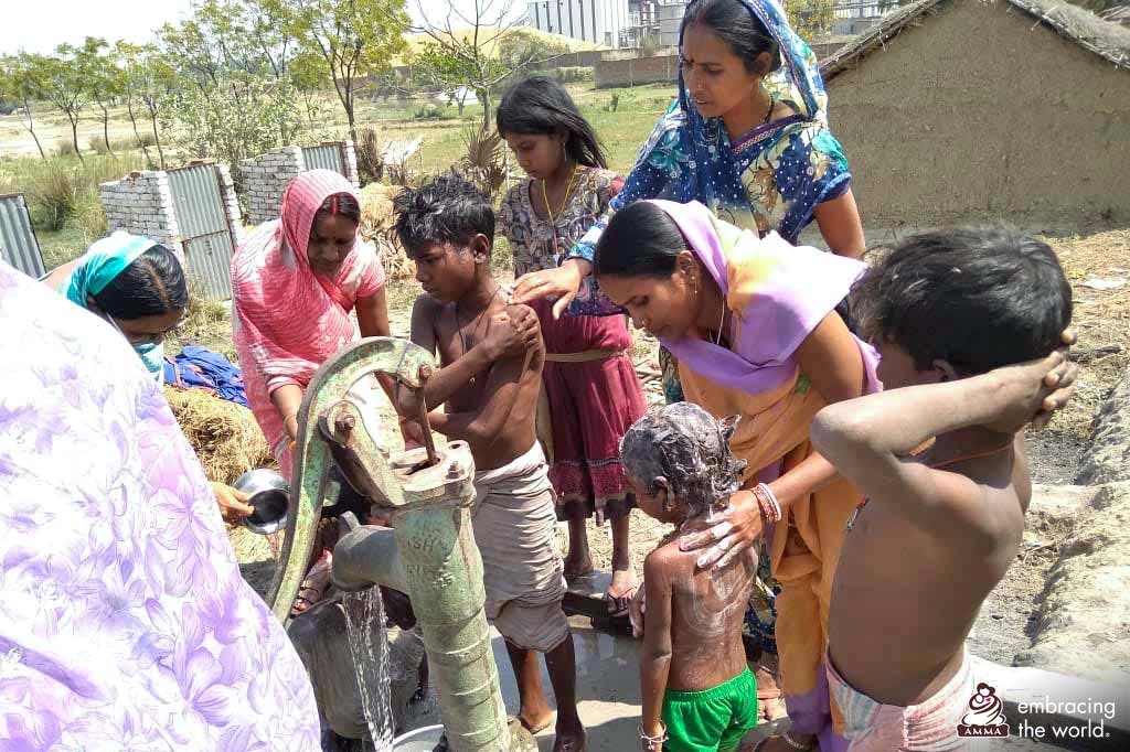 Children bathing outdoors around a communal water pump