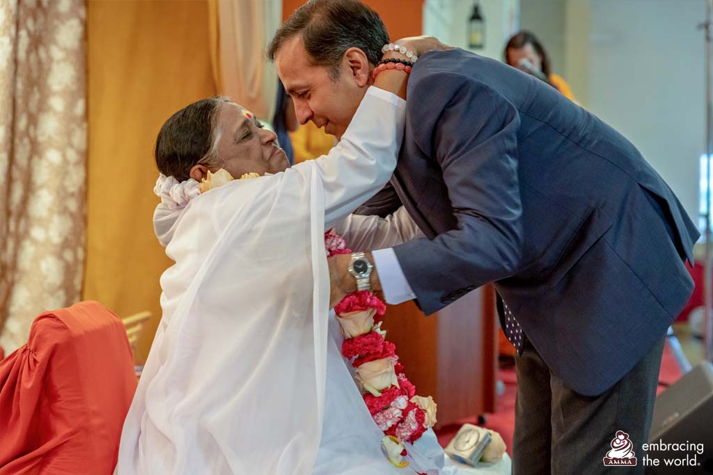 Congressman receives a hug from Amma. She is wearing the garland he just placed around her neck