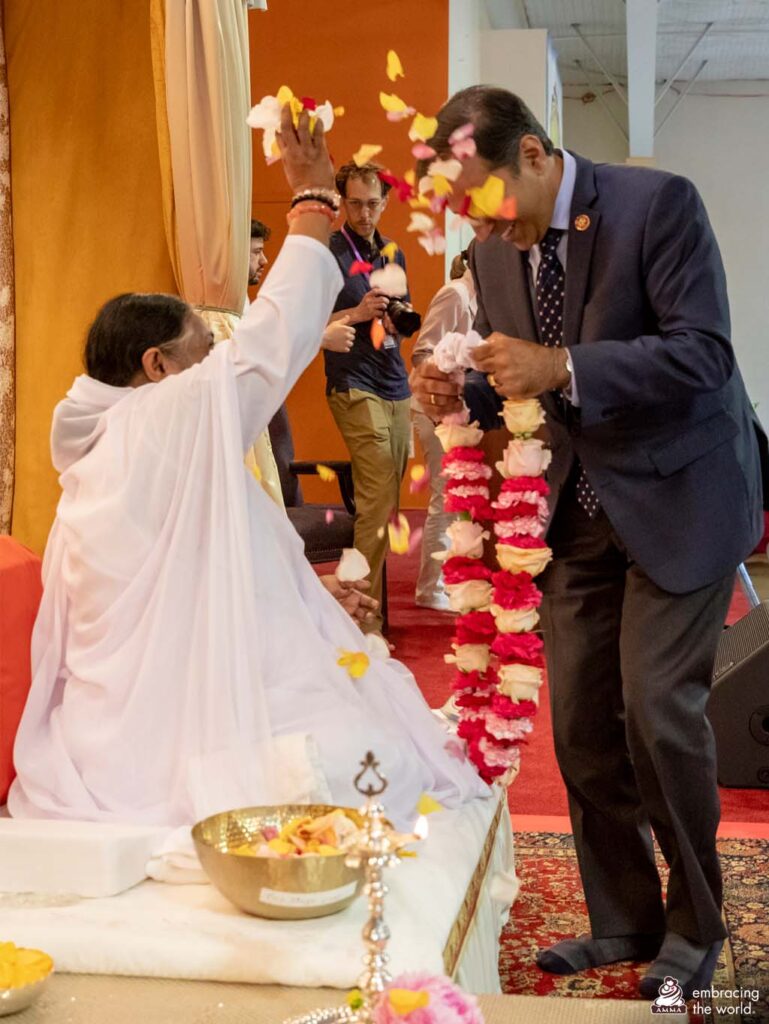 Amma throws flower petals on the congressman's head as he walks towards her with a garland