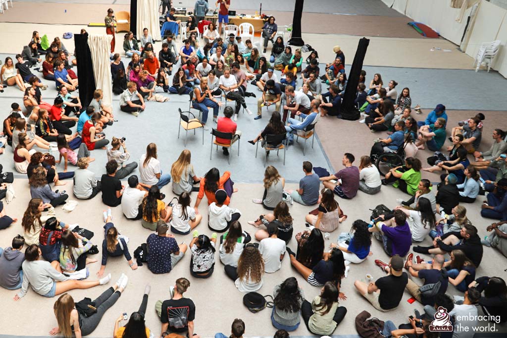 Large group of students sit in a circle listening to a discussion of a few people in the center