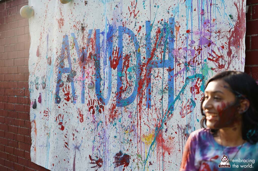 AYUDh member stands in front of an YUDh sign which has been painted with handprints