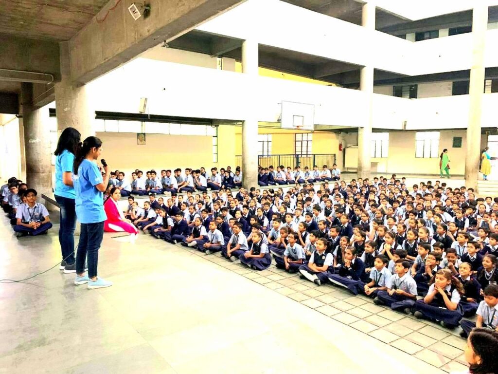 Two female AYUDH members share about Shivaratri on a stage overlooking a couple of hundered school students listening very attentively. 