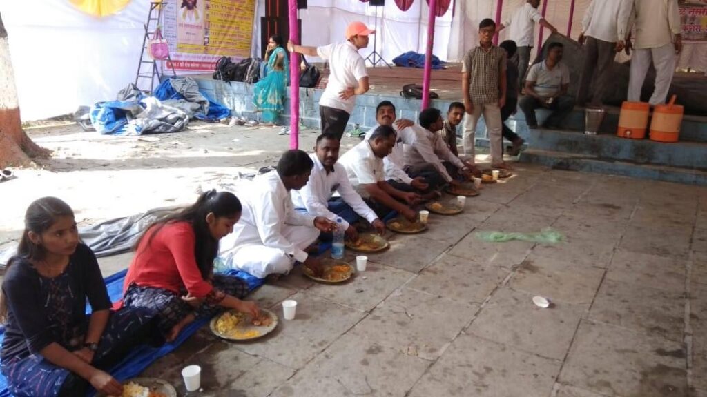 Devotees at the Shiva temple seated on the floor enjoy the prasad or blessed meal served by AYUHD.