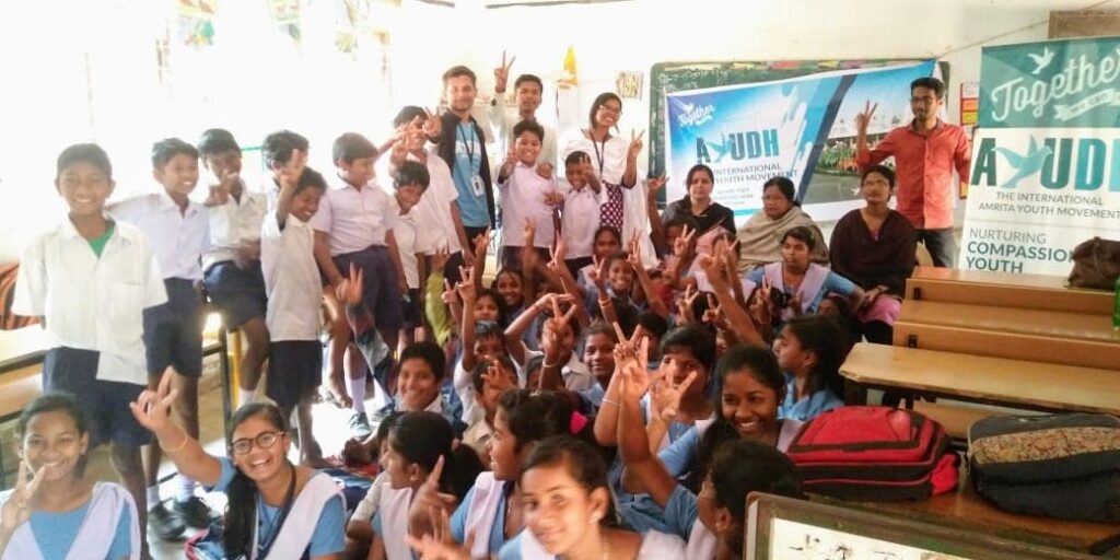 Gathered in a group, all of the students and AYUDH members show their hand gestures of a peace sign.