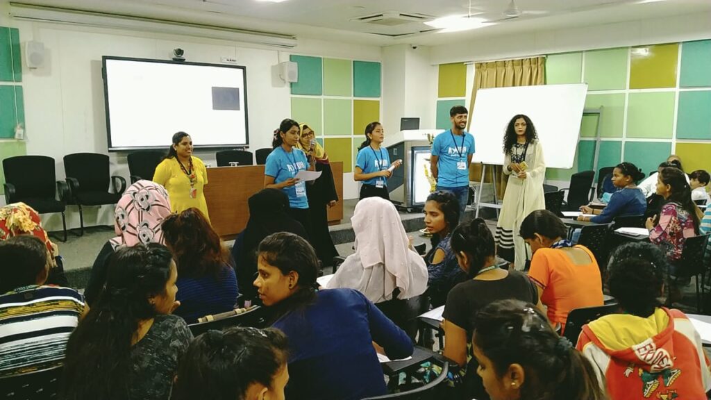 AyUDH members stand in the front of a modern ;college classroom, as the students at their desks listen.