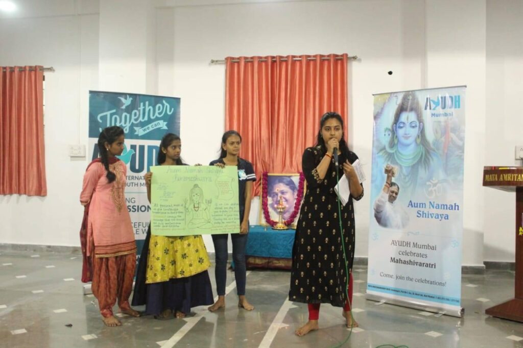 Three young women hold their poster board presentation as one woman talks with a microphone.