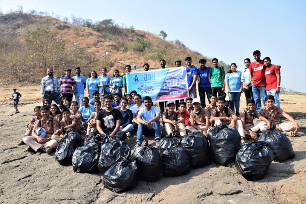 A large group of AYUDH Pune gathered around many big black bags of garbage collected.