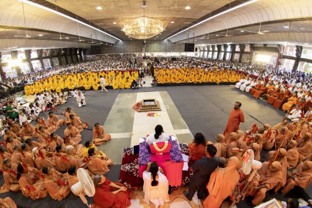 From behind, Amma is seated and the entire big hall is full of those attending the ceremony.