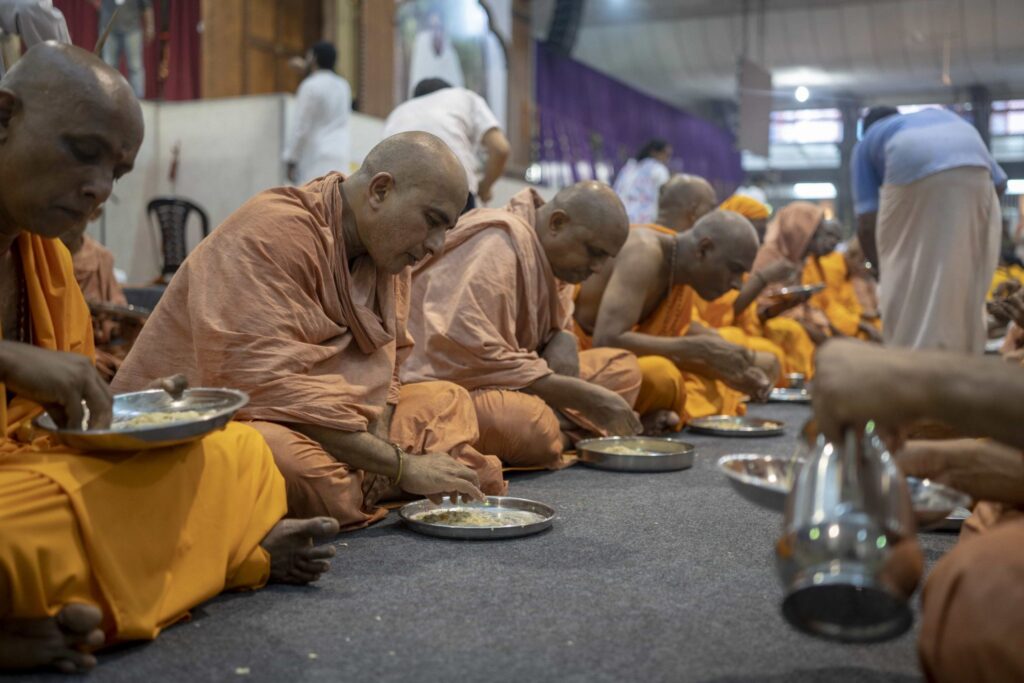 A line of seated male sannyasa intitiates eat the food cooked from their alms.