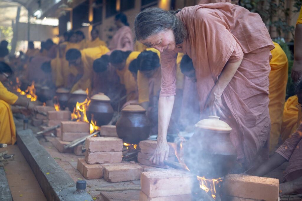 Swamini Ambikamrita Prana bends down to tend the fire, in the center of mounted bricks, for the cooking of the food.