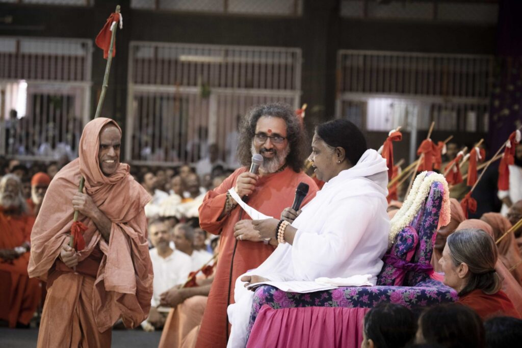 Amma pronounces the new name of a male sannyasa initiate, as he stands with his staff in hand.