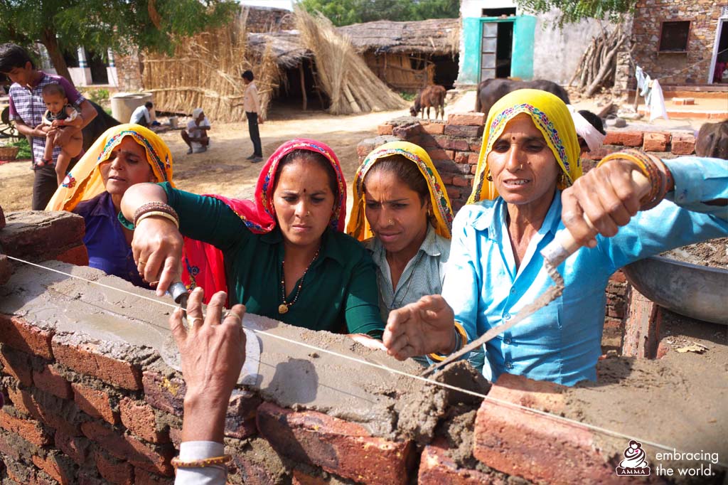 A group of women place cement on a wall of bricks