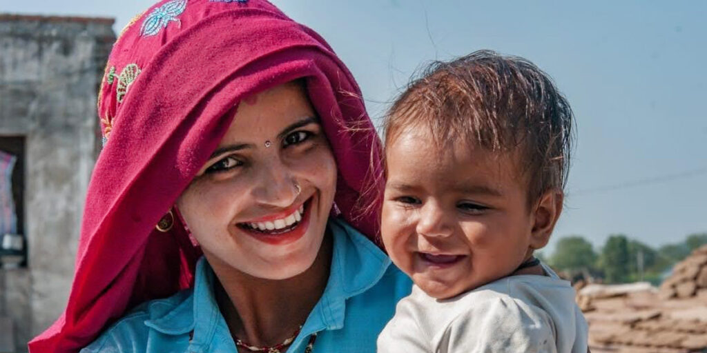 A village mother holds her small child, both smiling and happy.