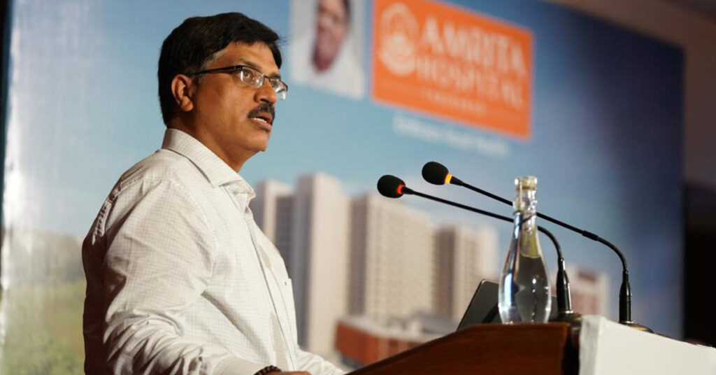 Standing at the podium, with Amma's picture and Amrita Hospital banner in the background, Dr. Singh addreses the audience.