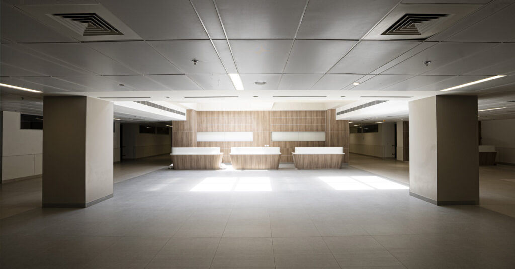 A wide view of the almost futuristic feel to the hospital interior with wide columns on each side and outpatient reception desks lit up in the distance. 