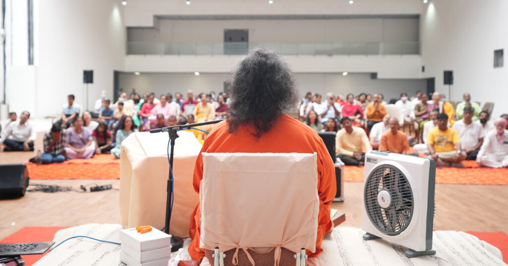 The hall is filled with people singing with Swamiji