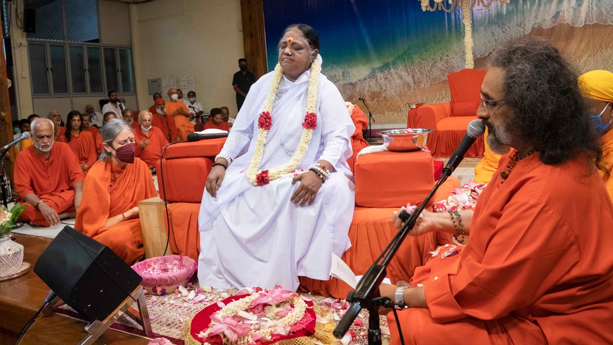 Amma sitting, surrounded by her senior disciples, as Swami Amritaswarupananda Puri holds flowers while conducting guru paduka puja.