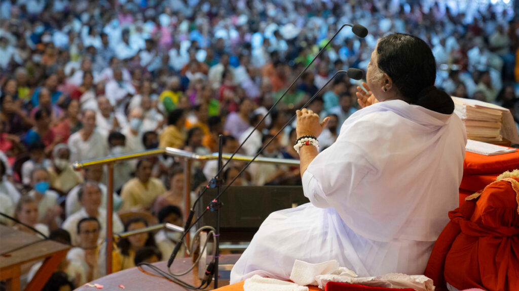 Amma speaking into a microphone as a crowd celebrating her birthday listens to her speak.