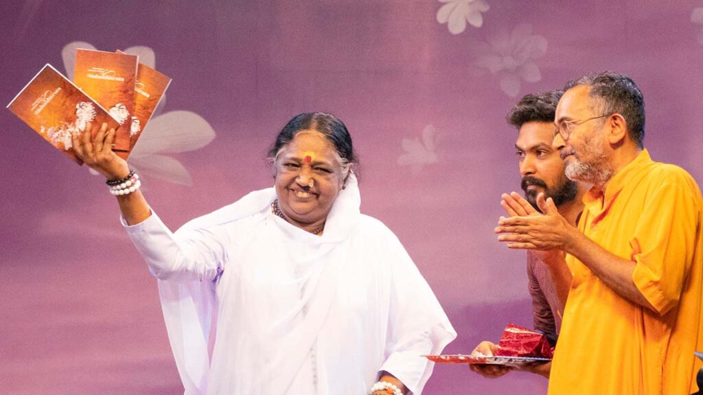 Amma holding up Strategic Lessons from Mahābhārata and smiling with Brahmachari Achyutāmṛta clapping for the launch of the new book of essays
