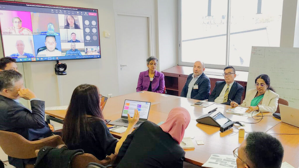 Gathered around and seated at a conference table with laptops and eager faces, team member discuss design solutions.