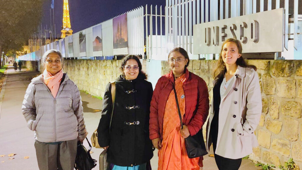 Amrita's team of four women, wearing winter jackets on a street in Paris, smile standing together.