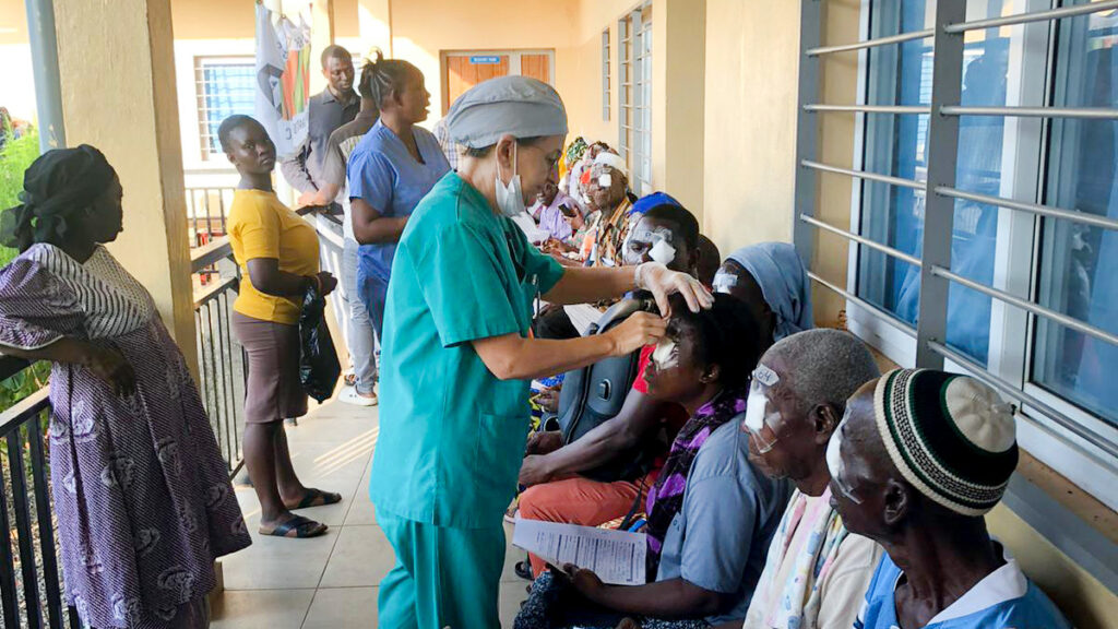 patients sitting in chairs outside the hospital while one of the doctors examines one of them