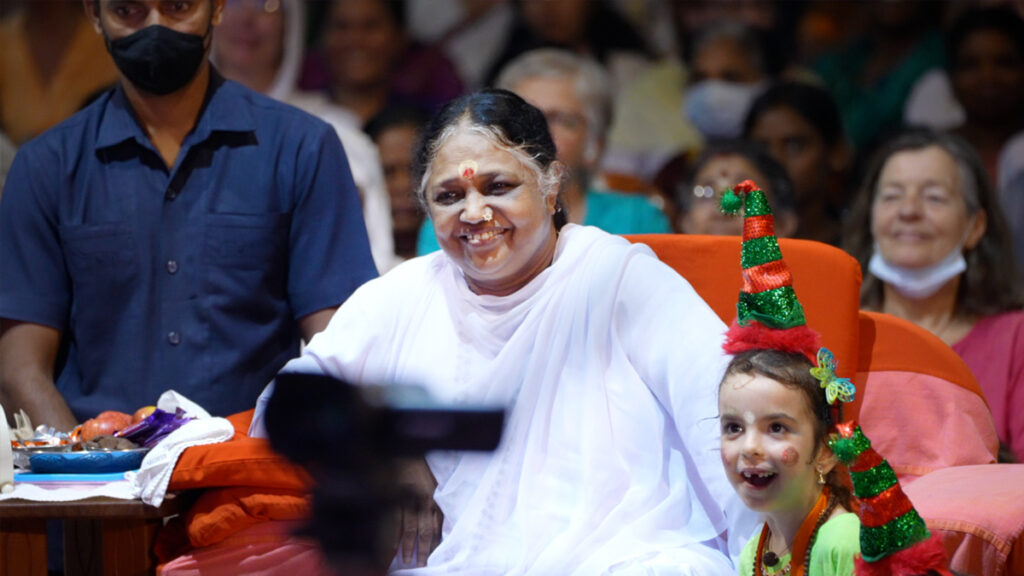 Amma sitting in her chair watching the performances with a small girl siting next to her.