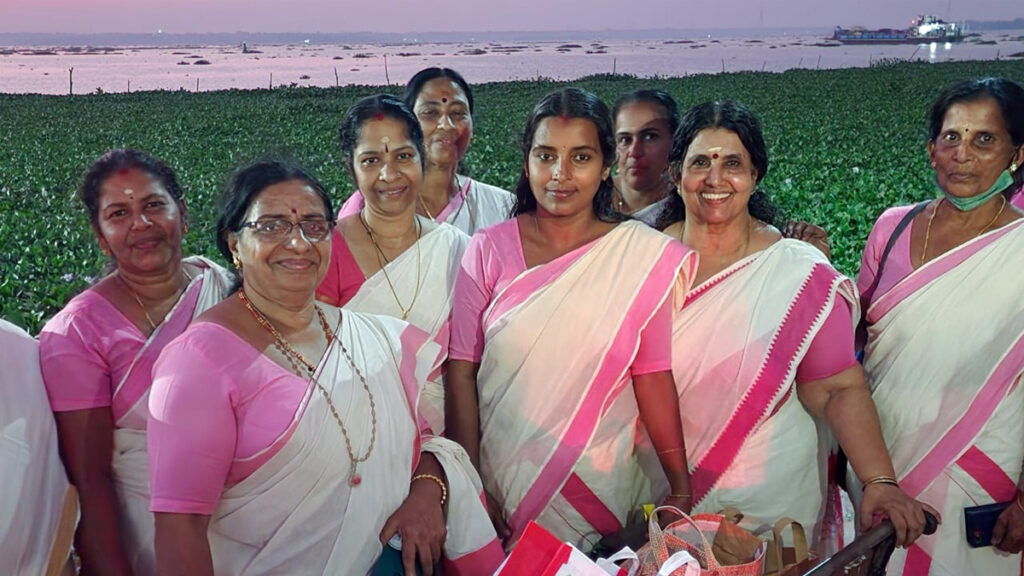 Women in white and pink saris stand together and smile