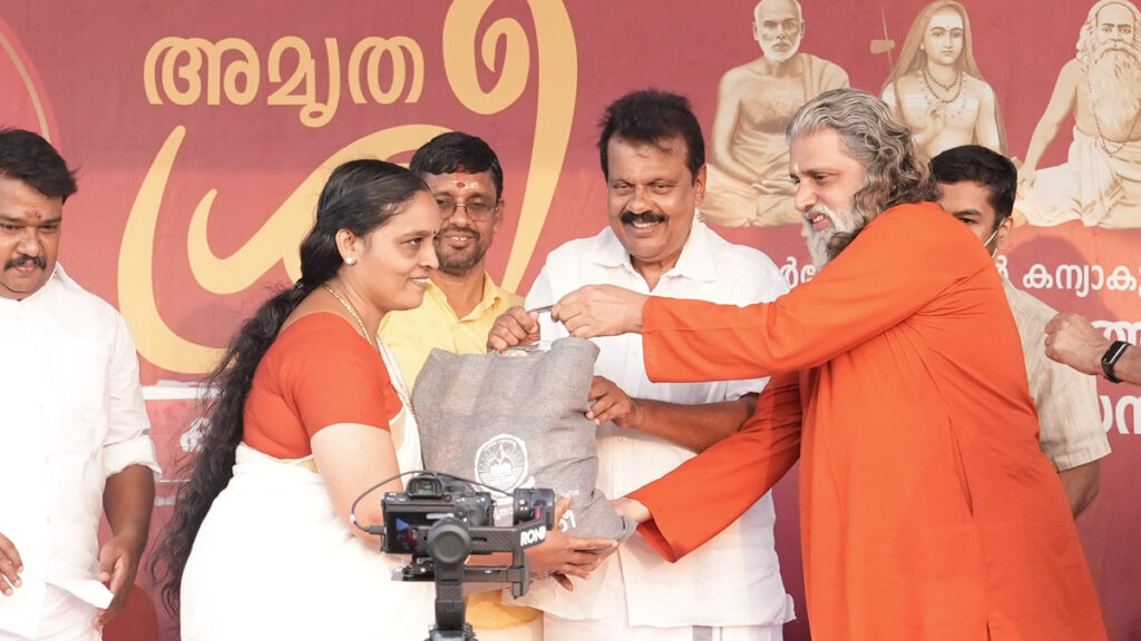 Swami Amritakripananda Puri and Sri NA Nellikunkun, MLA distributing a sack that held necessary supplies to a woman.