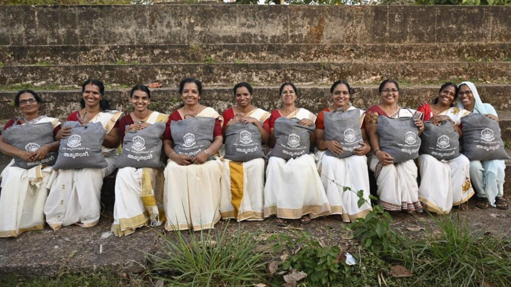 10 women sitting in a row smiling with their sacks of supplies on their laps.