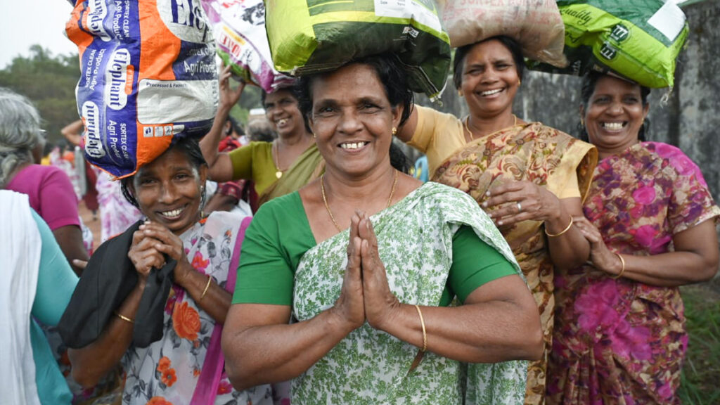 Women carry their new food supplies with folded palms and smiles