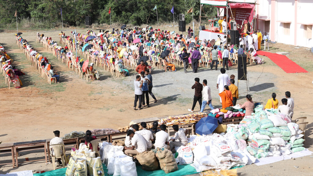 An outdoor meeting, with rows and rows of chairs filled with Amrita SREE self-help group women.  