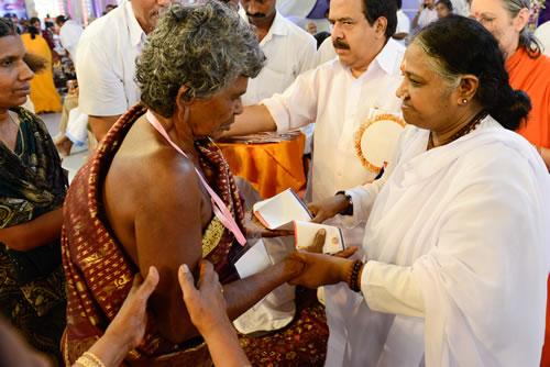 Amma hands over an envelope to an elderly woman on stage