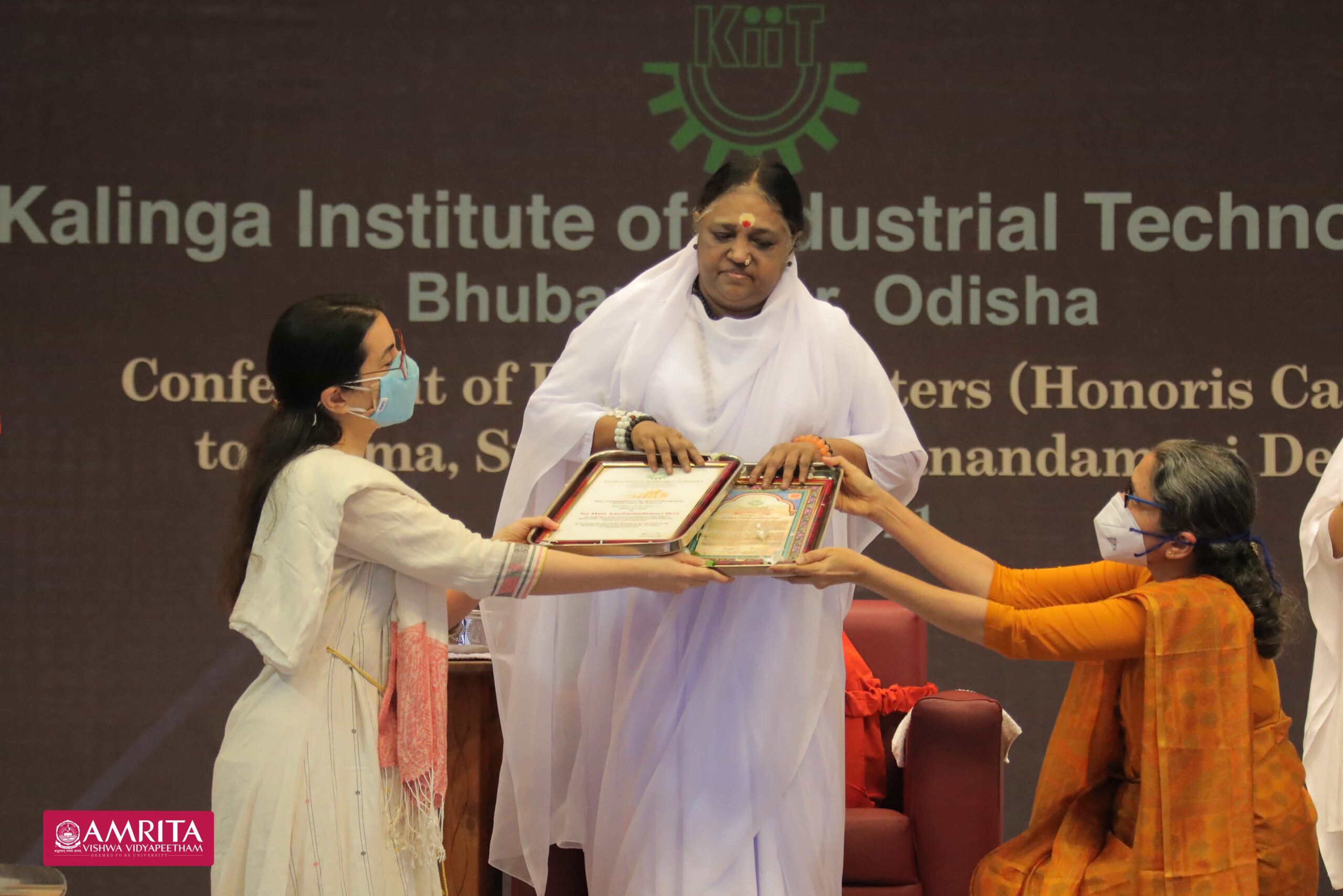 Amma receives Doctorate award while standing with presenters.