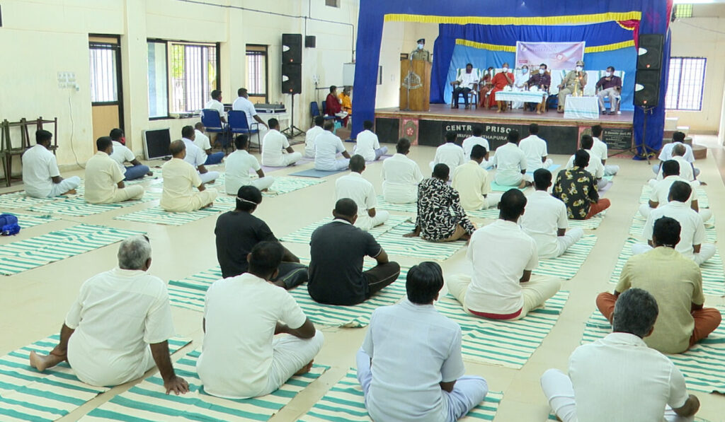 Rows of male prison inmates sitting on green and white striped mats listening to yoga instruction.