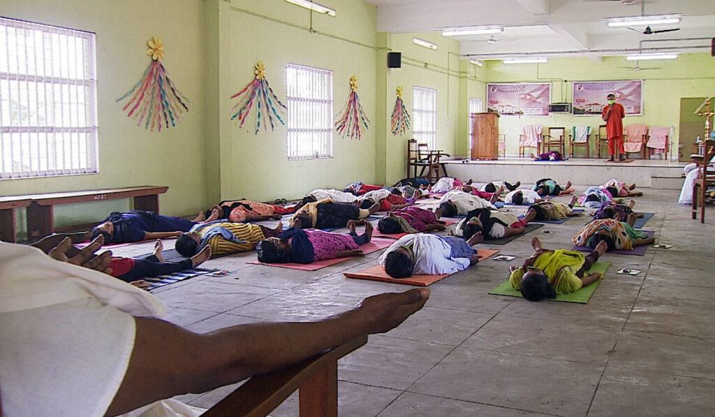 Female inmates all lie on the floor on their backs, in the final relaxation yoga posture called savasana.