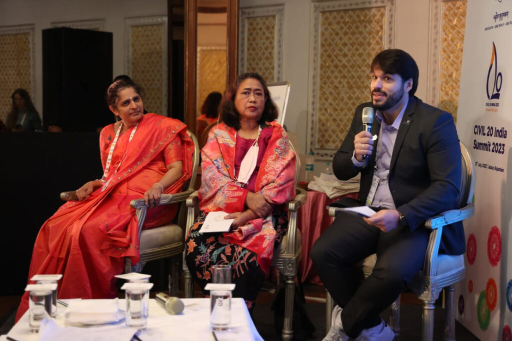 A seated speaker engages in discussion while two participants look on