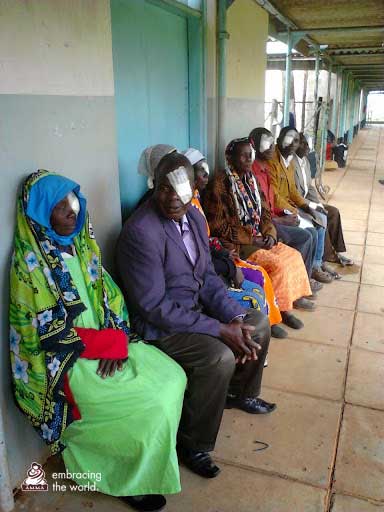 Patients sit in a line with bandages over their eyes