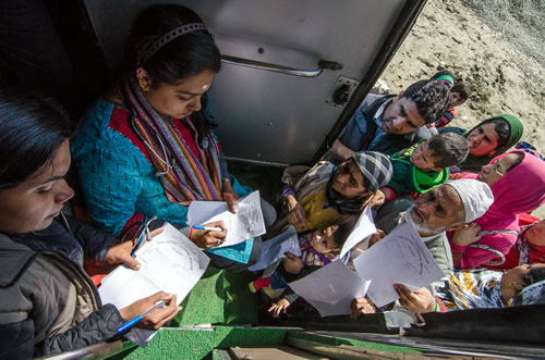 Villagers stand outside a vehicle, as healthcare workers look at paperwork