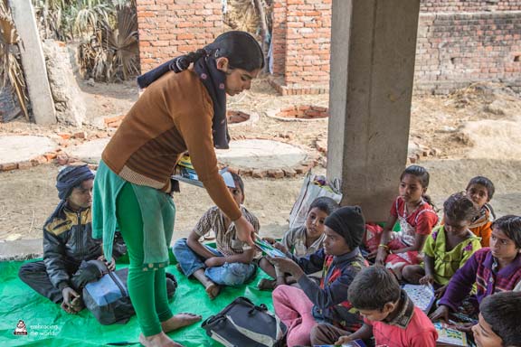 Indian woman passes out books to a group of children